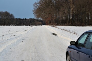 Blue car on snowy dirt road next to a field