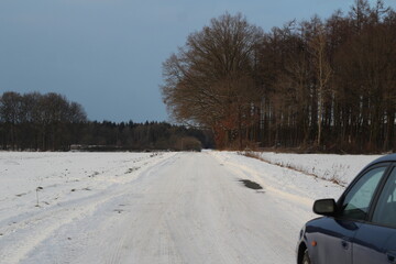 Blue car on snowy dirt road next to a field