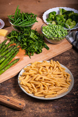 Ingredients for making primavera pasta on a wooden table - casarecce pasta, asparagus, beans, broccoli and peas