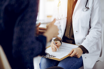 Doctor and patient discussing current health examination while sitting in sunny clinic. Medicine...