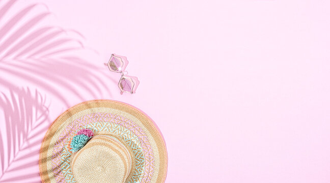 Round summer hat with accessories on pink background, with palm leaf&rsquo;s shaddow