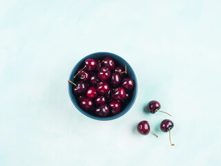 Fresh summer cherries in bowl on turquoise background.