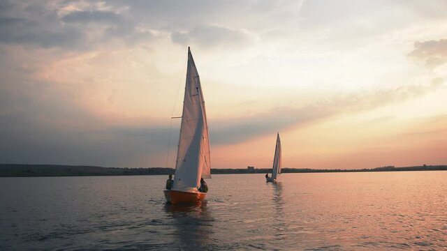 Sailboat. Men in life vests sailors team sailing across wide lake scenery. Beautiful seascape, water landscape abd sunset with white yachts.