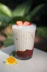 Strawberry milk with fresh strawberries in a glass placed on a white table.
