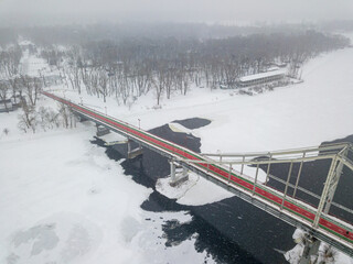 Footbridge across the Dnieper river in Kiev. Aerial drone view. Snowy winter morning, blizzard.