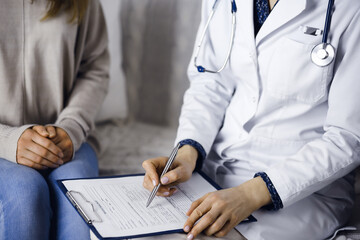 Unknown woman-doctor and patient discussing current health examination while sitting indoors. Stay...