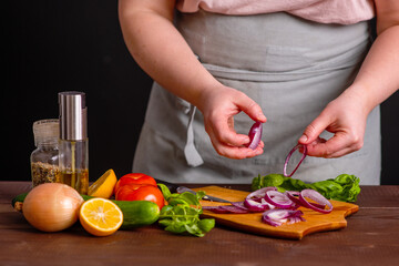 The chef cuts fresh vegetables on a wooden board. Cooking a burger.
