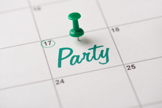 Green beer party is almost here concept. Cropped close up view photo of thumb tack attached to white calendar with word party