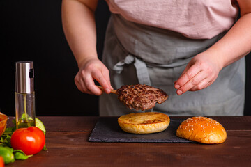 A close-up of a delicious burger being prepared. The cook puts a juicy fried cutlet on top of a toasted bun. Gastronomy, recipes, menus, fast food. Juicy burger