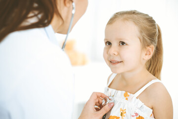 Obraz na płótnie Canvas Doctor examining a little girl by stethoscope. Happy smiling child patient at usual medical inspection. Medicine and healthcare concepts