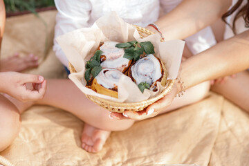 Obraz na płótnie Canvas Female hands holding out a basket of cinnabon buns. Dessert during a picnic.