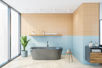 Blue and beige tiled bathroom with bathtub near window and sink