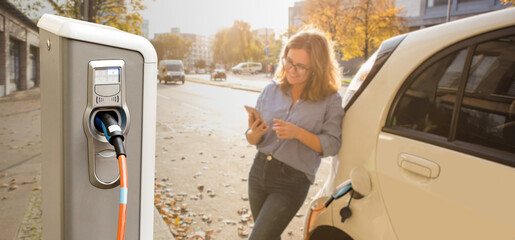 Close up of charging station on a background of a woman with a smartphone near an electric car	