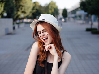 Happy woman in a white hat and glasses walks in nature on the street