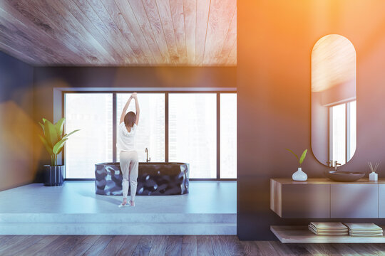 Black and wooden bathroom with bathtub and sinks, woman near window