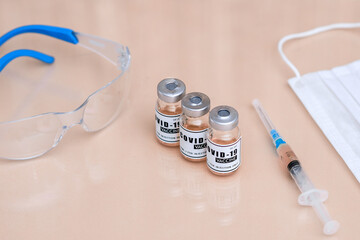 A bottle of of coronavirus vaccine. a dialed syringe on the table. Vaccine and ampoule, safety glasses, a medical mask. Vaccination against COVID-19.