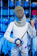 Young guy in a fencing suit with a sword in his hand, on a blue background, neon light. The athlete...