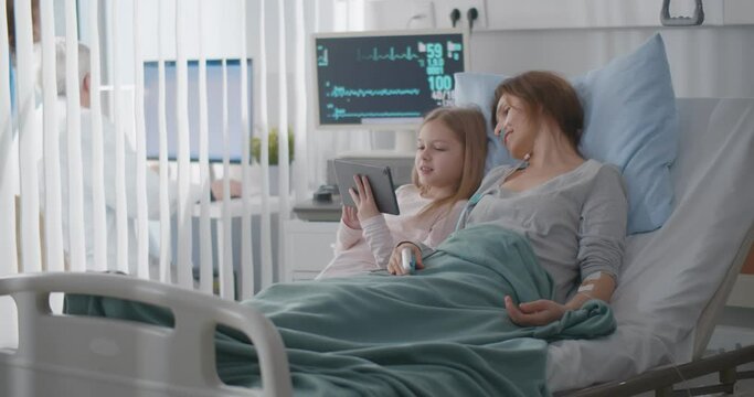 Little girl visiting sick mother in hospital showing photo on digital tablet