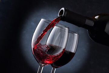 Red wine is poured into a glass from a bottle on a blurry blue background, a stream of red wine...