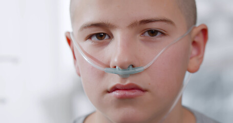 Close up portrait of sad sick boy with nasal cannula looking at camera in hospital - obrazy, fototapety, plakaty