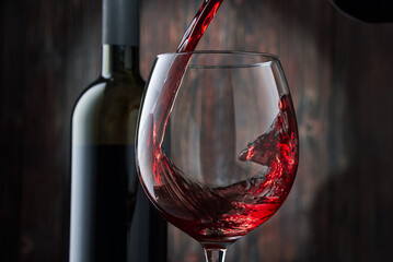 Red wine is poured into a glass from a bottle on a blurred wooden background, a stream of red wine...