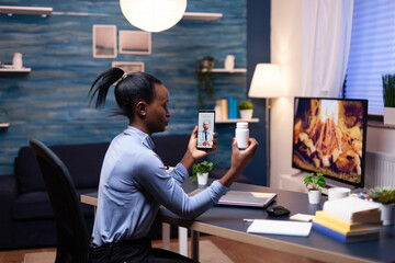Doctor explaining treatment to dark skinned woman during video call late at night while she's holding pills bottle. Black patient in a video call with medic discussing health problems of woman.