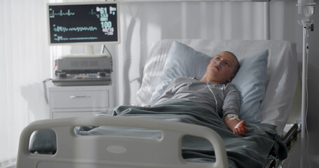 Unhappy sick kid with cancer lying in hospital bed