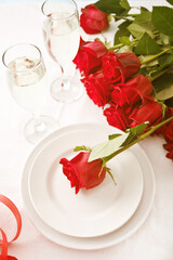 Romantic restaurant table setting for two with roses, plates and glasses.