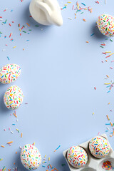 Easter frame made of colorful eggs bunny, sweets on pastel blue background. Flat lay, top view, copy space. Happy Easter vertical banner design.