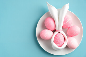 Stylish Easter table setting with easter bunny napkin and pink eggs on plate on turquoise background. Flat lay, top view.