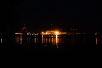 Fototapeta na wymiar View of the thermal power plant from the bank of the reservoir at night. A lot of backlighting in different colors.