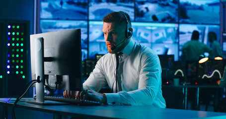 Male operator using computer in surveillance center - obrazy, fototapety, plakaty