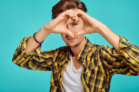 Young man shows heart sign, blue background