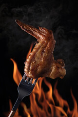 Hot bbq chicken wing on a fork on the background of an open fire. The meat gives off smoke.