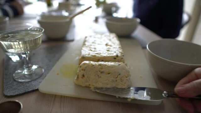 Close up footage of a ice cream passionfruit cake being sliced, cut and served in a bowl as dessert at a family meal time. Daytime footage of mealtime with plates, bowls, glasses on kitchen table