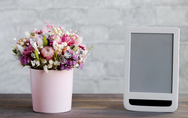 A bouquet of dried flowers in a pink vase and a tablet with a blank screen close-up against a brick wall. Mockup concept for ordering flowers online