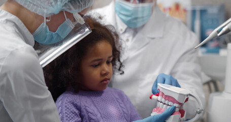 Dentist teaching cute afro-american little girl how to brush teeth