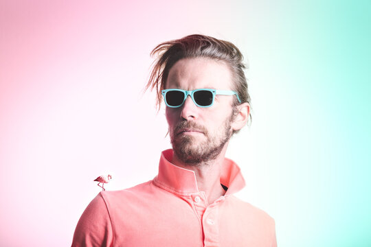 Portrait of adult man with blue sunglasses and flamingo on his shoulder with pastel color background