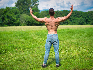 Back of Muscular Shirtless Young Hunk Man Outdoor in Nature Standing on Grass. Showing Healthy...