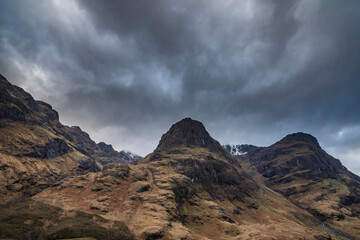 Majestic moody landscape image of Three Sisters in Glencoe in Scottish Highlands on a wet Winter day wit high water running down mountains