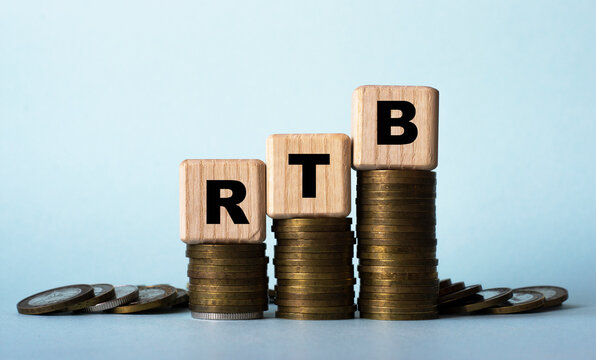 RTB - acronym on wooden cubes. Which stand on stacks of coins on a light background