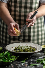 Chef hands cooking Penne vegan pasta with fresh spinach leaves. sprinkling cheese on green pasta with spinach and green pesto, vertical image, place for text