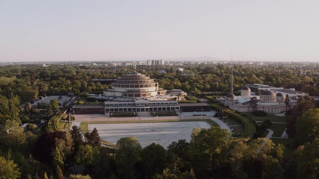 Aerial shot of a beautiful park with large, modern building in the middle. Round, huge architecture in a green city. Urban landscape drone shot.