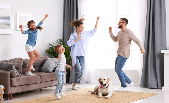 Playful family dancing in living room with dog