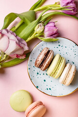 Colorful french macaroons with tulips and rose on pink background