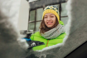 Girl with emotional face cleaning the windshield of a car from snow.