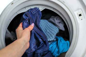 Female hand getting out clean jeans clothes from a washing machine at home