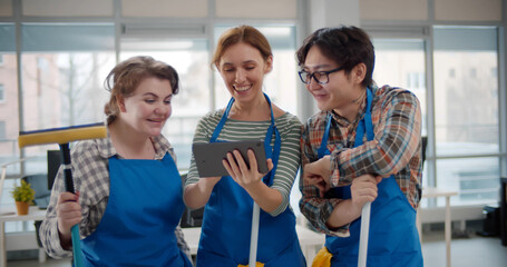 Professional janitors in aprons using tablet pc working in office
