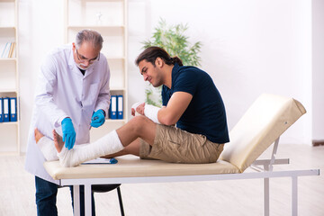 Obraz premium Young injured man visiting old doctor traumatologist