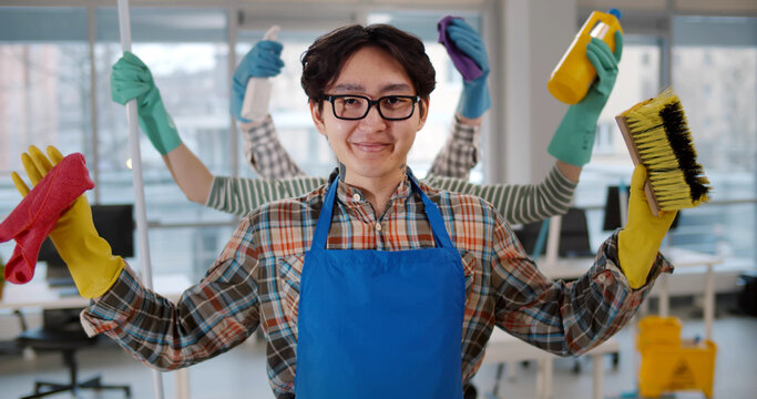 Portrait of asian multi-armed man janitor holding cleaning equipment and smiling at camera